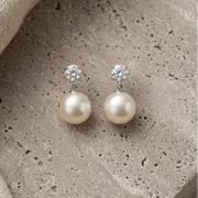 Pair of pearl earrings with clear gemstones on a textured stone surface.